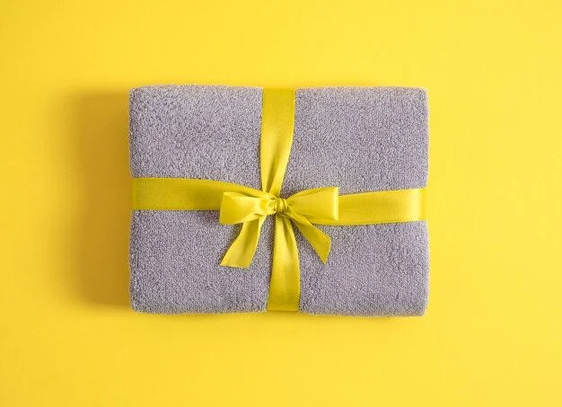 grey terry towel folded against yellow background towel stacked tied by yellow ribbon isolated 113707 199 e1659547413823 Home Gift Towels